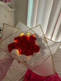 someone is holding a heart shaped box with roses in it and lit candles on the inside