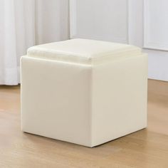 a white square ottoman sitting on top of a hard wood floor next to a window