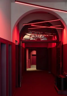 an empty hallway with red lighting on the ceiling and carpeted flooring in front of it