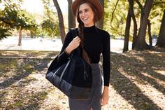 a woman wearing a hat and carrying a black bag in the park on a sunny day