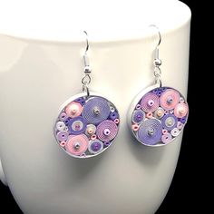 a pair of purple and pink earrings sitting on top of a white cup