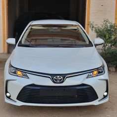 the front end of a white car parked in front of a garage with its door open