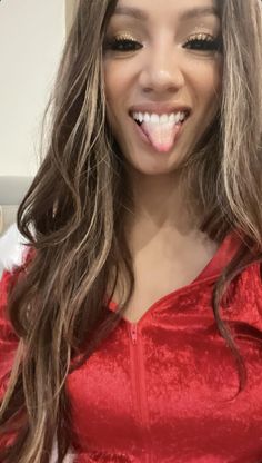 a woman with long brown hair wearing a red top and gold eyeshadow is making a funny face