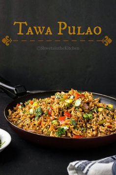 a pan filled with rice and vegetables on top of a black table next to plates