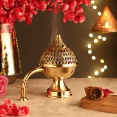 a brass oil burner sitting on top of a table next to flowers and a cutting board