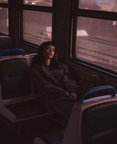 a woman sitting on a train seat looking out the window at the street below her