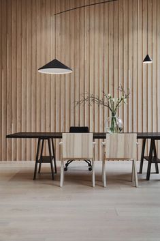 a dining table with two chairs and a vase filled with flowers in front of a wooden wall