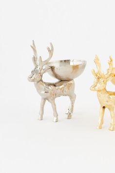 two silver and gold deer figurines sitting next to each other on a white surface