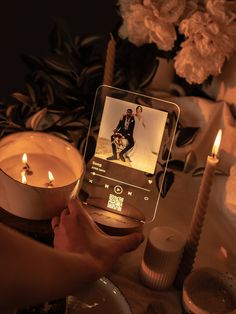 a person holding a cell phone in front of a table with candles and pictures on it