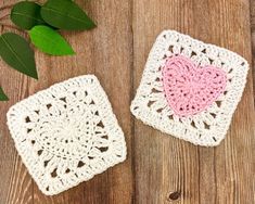 two crocheted coasters with a pink heart on them next to green leaves