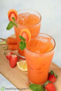 two glasses filled with orange juice and garnished with strawberries on a cutting board