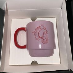 a pink and red coffee mug in a white box with the letter c on it