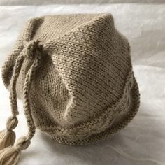 a knitted bag sitting on top of a white sheet with a tasseled handle