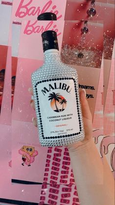 a person holding up a bottle of malibu rum in front of pink and white photos