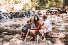 a woman and two children sitting on a log next to a waterfall with a dog