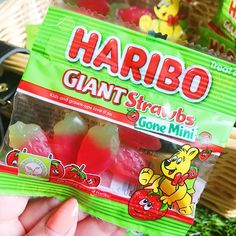 a hand holding a bag of gummy bears in front of a basket full of candy