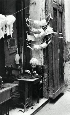 an old black and white photo of a man sitting in front of a sewing machine