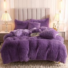 a bed with purple comforter and pillows on top of it in a room next to two lamps