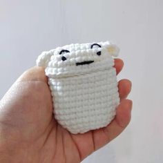 a hand holding a small crocheted white cup with eyes and nose on it