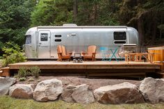 an airstream sits in the middle of a wooded area with picnic tables and chairs