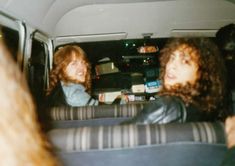 two women sitting in the back seat of a car, one with long curly hair