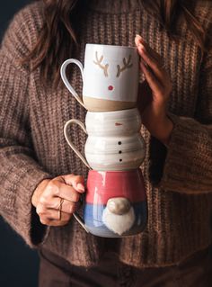 a woman holding a stack of coffee mugs with reindeer faces on them, all stacked together