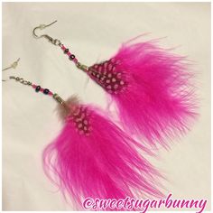 two pink feathers are hanging from hooks on a white background with black beads and silver earwires