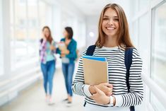 a woman is holding a folder and smiling at the camera while two other women are walking behind her