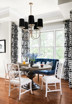 a dinning room table and chairs in front of a window with black and white curtains