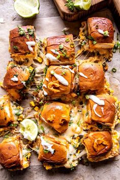 several small sandwiches with toppings on top of a wooden cutting board next to lime wedges