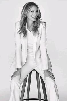 a black and white photo of a woman in a suit sitting on a bar stool