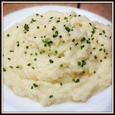 mashed potatoes on a white plate with green onions sprinkled over them and garnished with chives