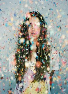 a woman with long hair standing in front of confetti falling from the sky