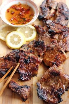 chopsticks and meat on a cutting board with lemon wedges