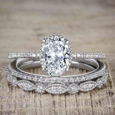 two wedding rings with an oval shaped diamond in the center, on top of a wooden surface