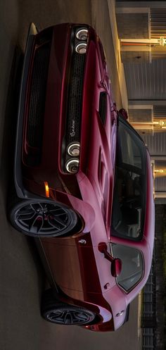 the front end of a red sports car parked in a parking garage next to a building