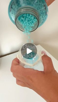 a person is pouring blue beads into a container with the lid down and their hands are holding it