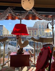 a red lamp sitting on top of a table in front of a window next to a chair