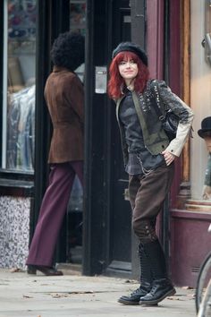 a woman with red hair is standing on the sidewalk in front of a storefront