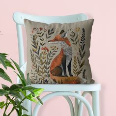 a pillow with a fox on it sitting next to a chair and potted plant