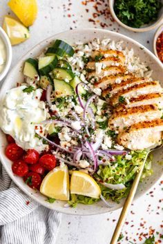 a white bowl filled with chicken, cucumber, tomatoes and other food items