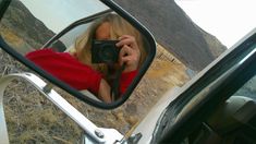 a woman taking a selfie in the side mirror of a car