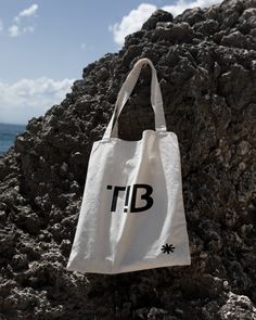 a white tote bag sitting on top of a rocky cliff next to the ocean