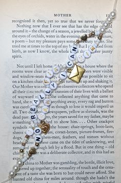 an open book with a bracelet made out of beads and charms on it's side