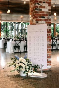 a table is set up with white flowers and greenery in front of a brick pillar