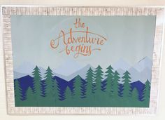 the adventure begins sign is displayed in front of a wall with mountains and pine trees