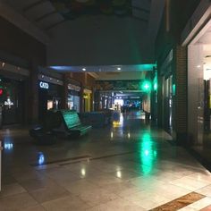 an empty shopping mall at night time with green lights on the benches and people walking by