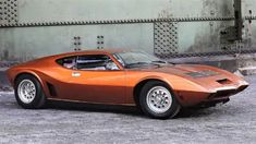 an orange sports car is parked in front of a concrete wall and some metal grates