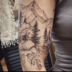 a woman's arm with mountains and trees tattooed on the back of her arm