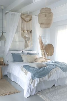 a bed with white sheets and pillows in a bedroom next to a wall hanging from the ceiling